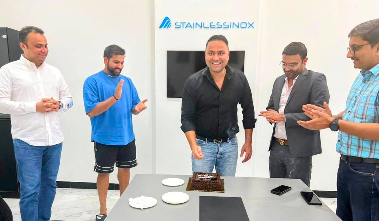Several men gathered around a celebratory cake, smiling and chatting at a party