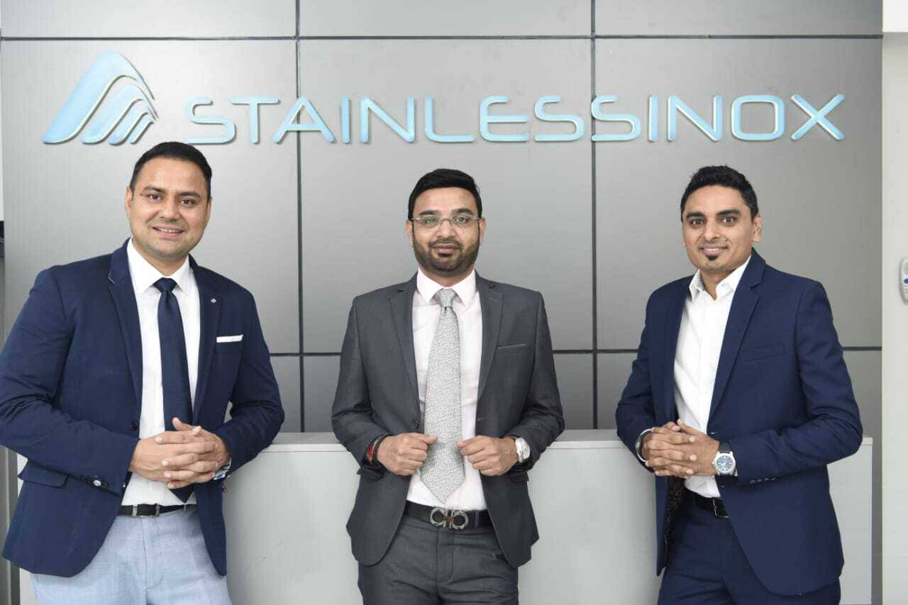 Three men in suits standing in front of the stainless sinx logo