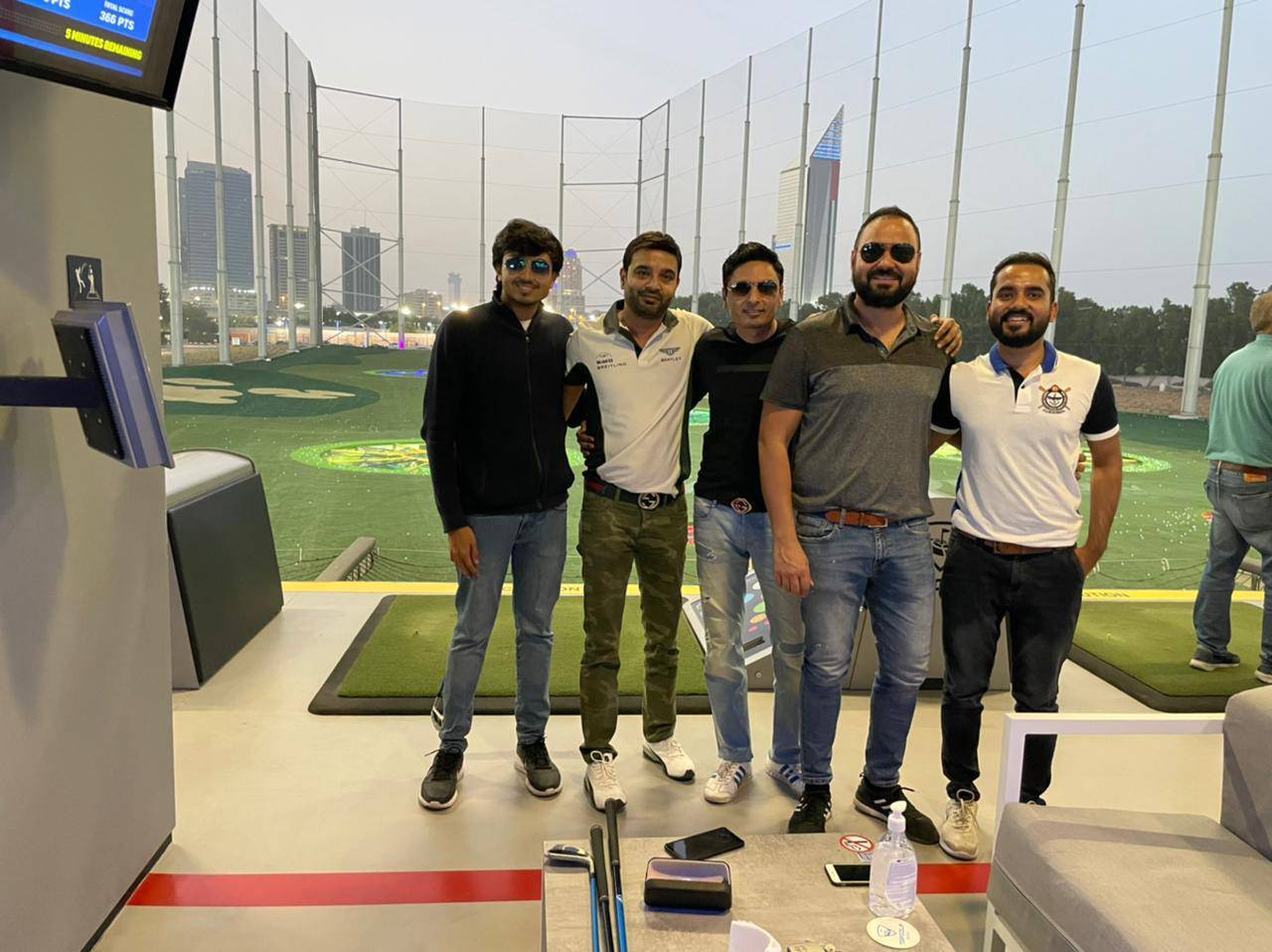 Four men smiling and posing for a photo inside a golf simulator, enjoying a game of golf together
